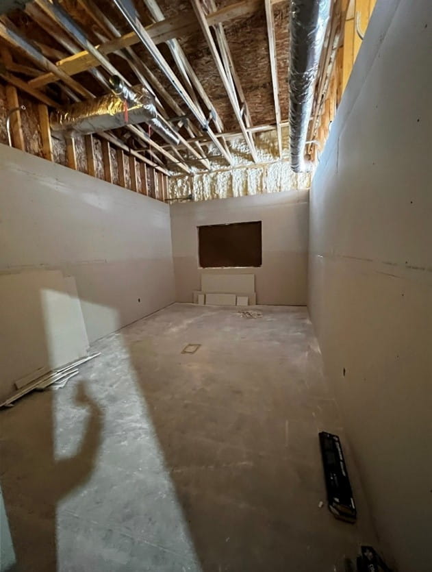 A room with exposed ceiling, a concrete floor and new drywall. 