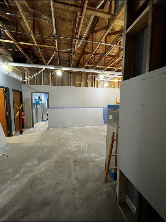 A large room with exposed ceiling, concrete floor and new drywall on the walls.