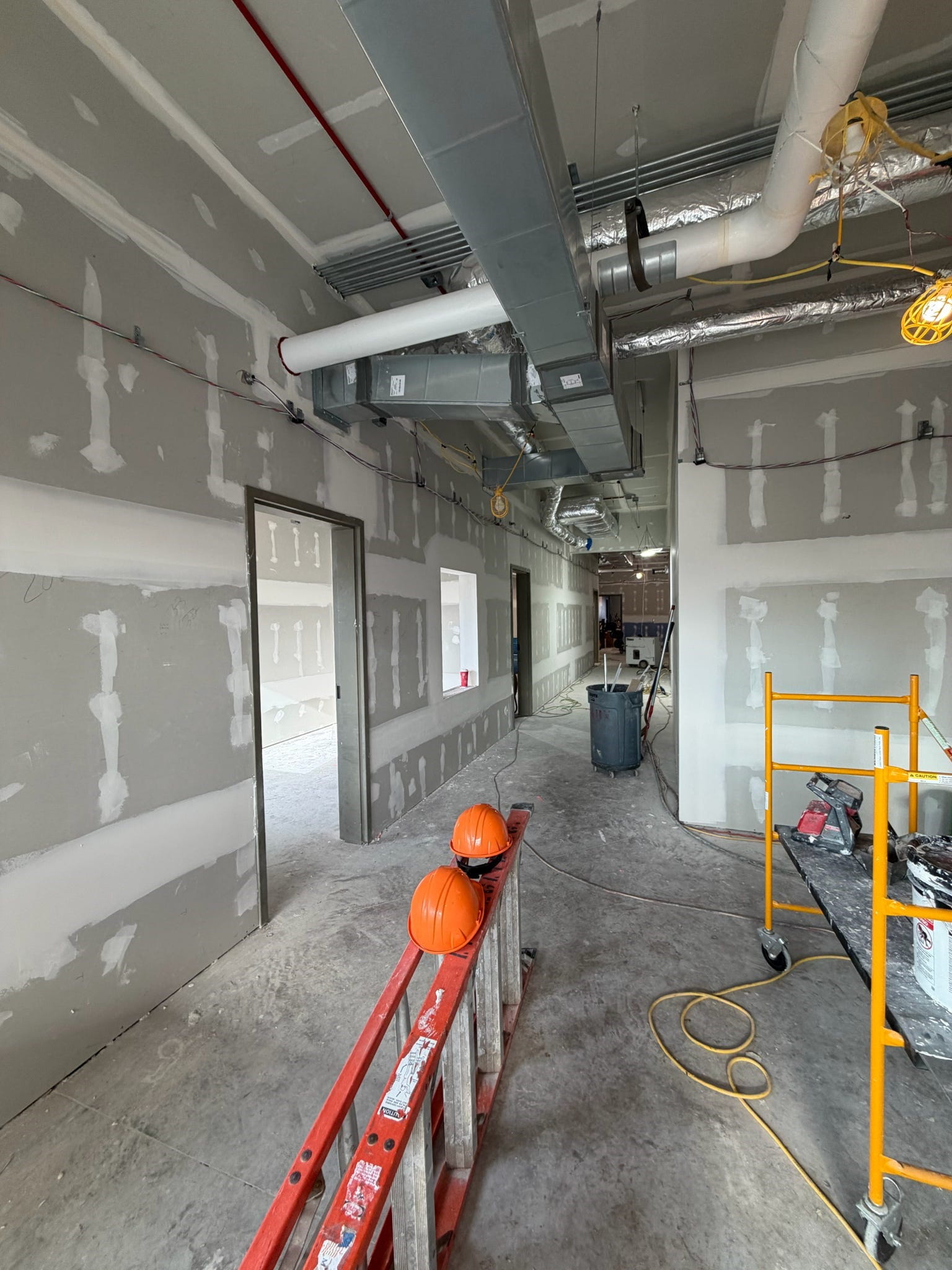 The lobby of the building with new drywall and unfinished floor. There are two doorways on the left and construction equipment in the middle of the room.