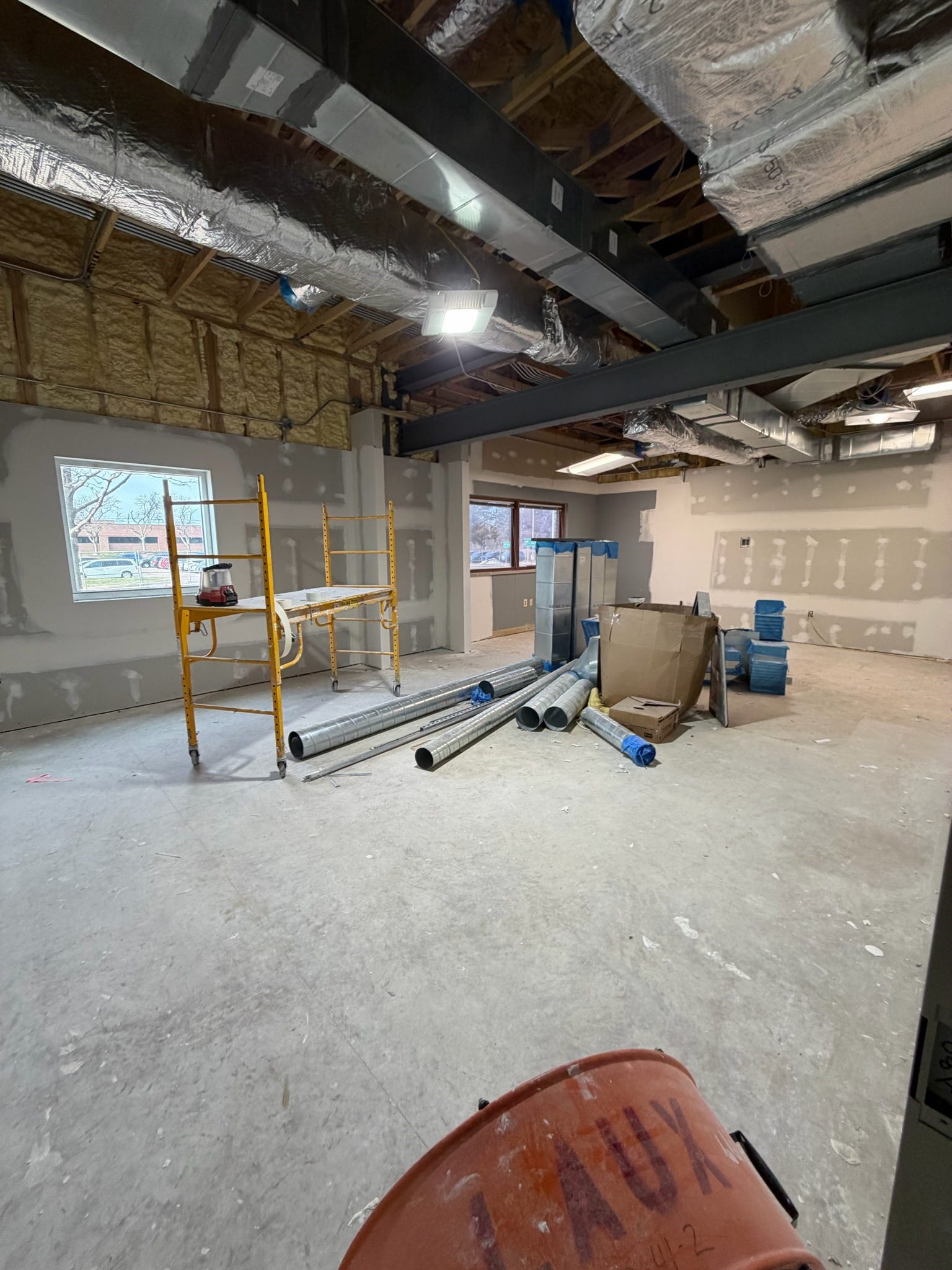 The conference room with new drywall, unfinished floor, and exposed ceiling. There is construction equipment in the middle of the room.