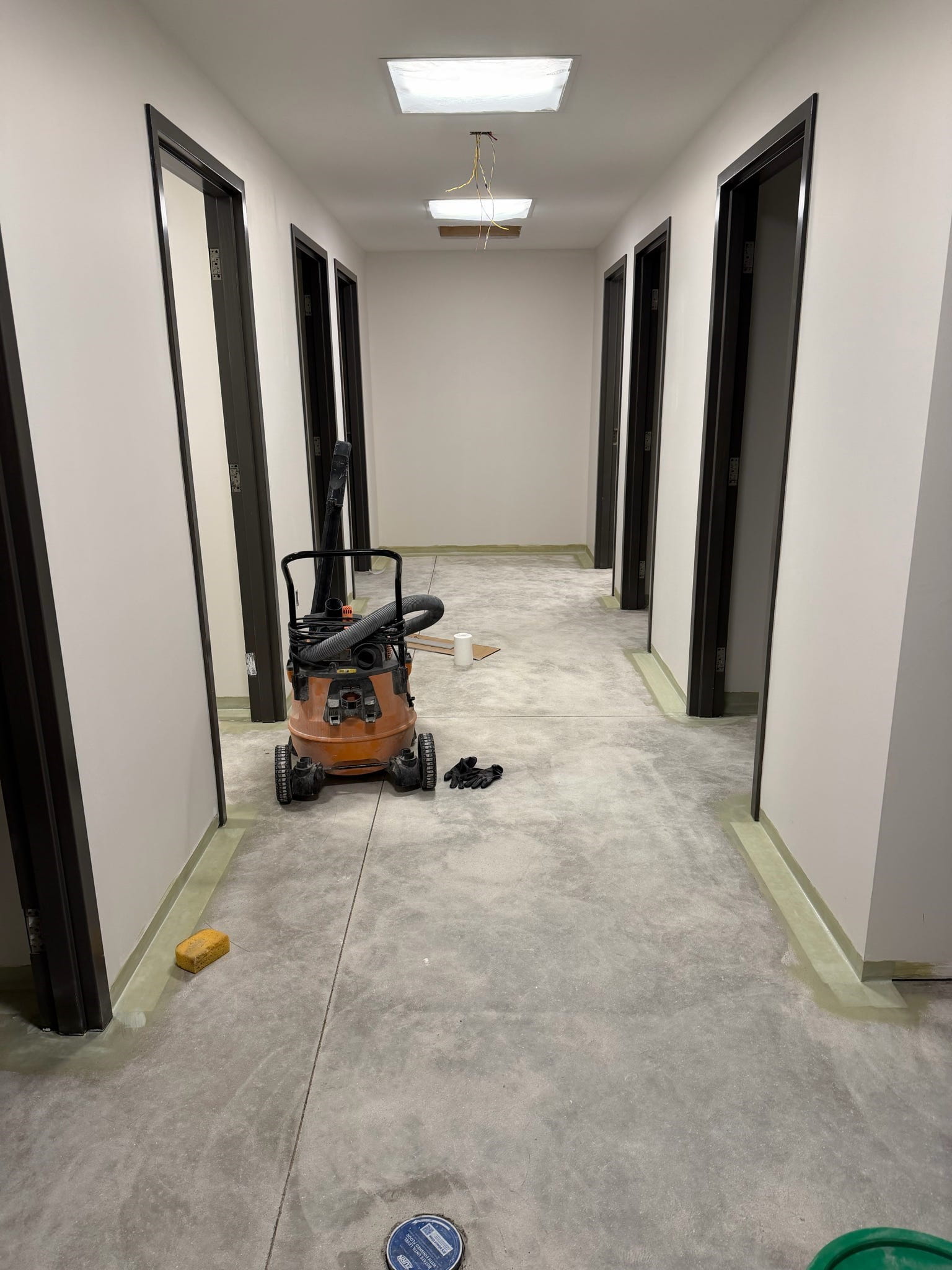 A hallway with new drywall and unfinished floor and doorways on each side that open into the new restrooms. 