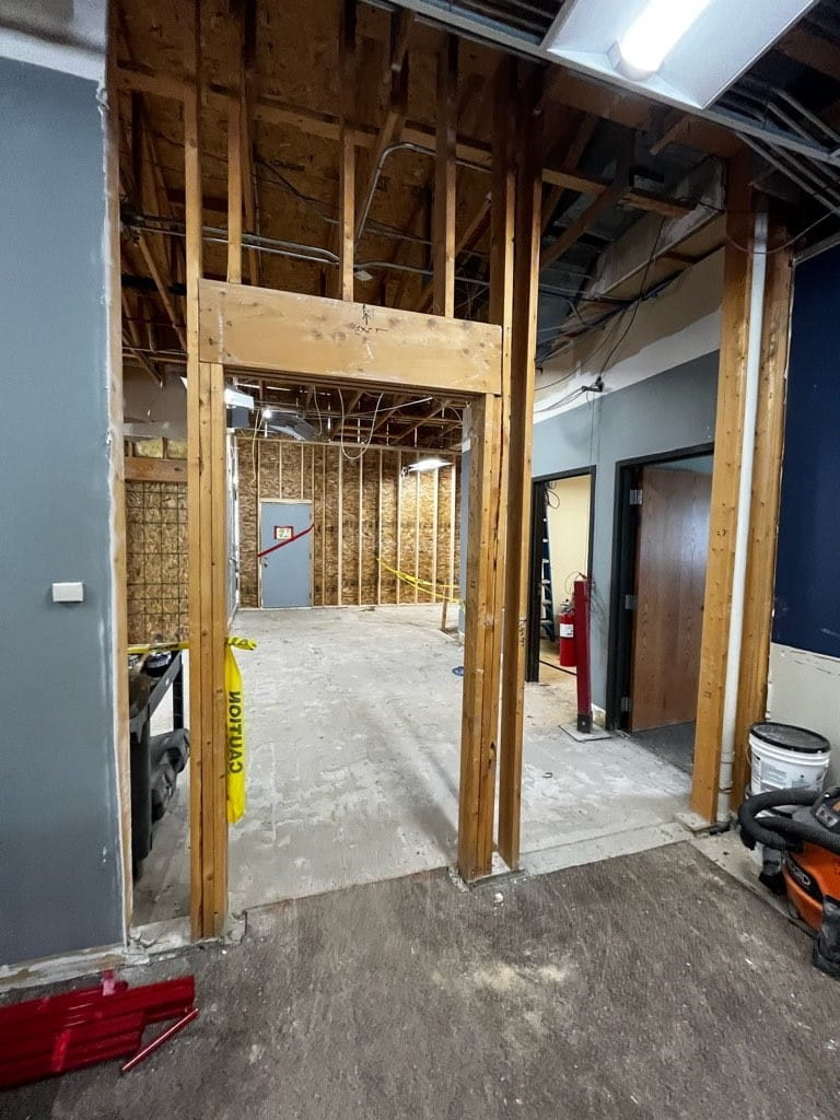 A doorframe in an unfinished room looking into the unfinished lobby with cement floor and exposed walls and ceiling