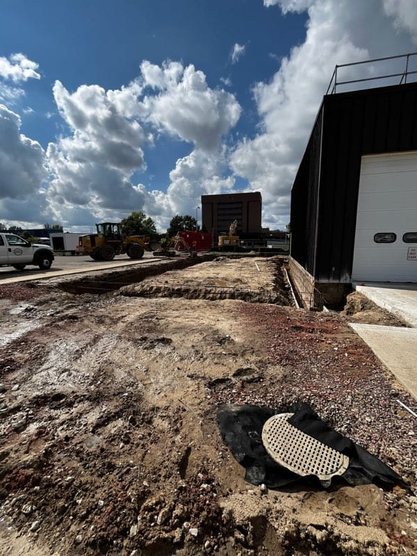 A dirt area next to the building where a rectangle trench has been dug out. Construction vehicles are in the background.
