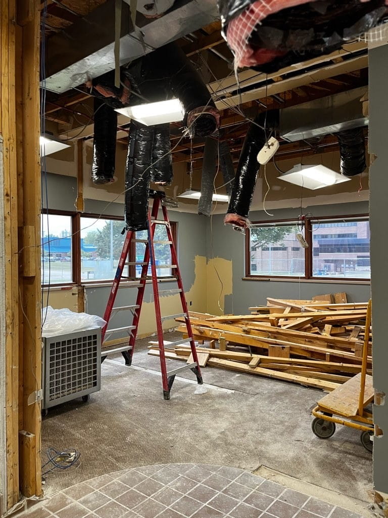 A ladder and pile of wood underneath a ceiling that has been removed, exposing airducts and wiring