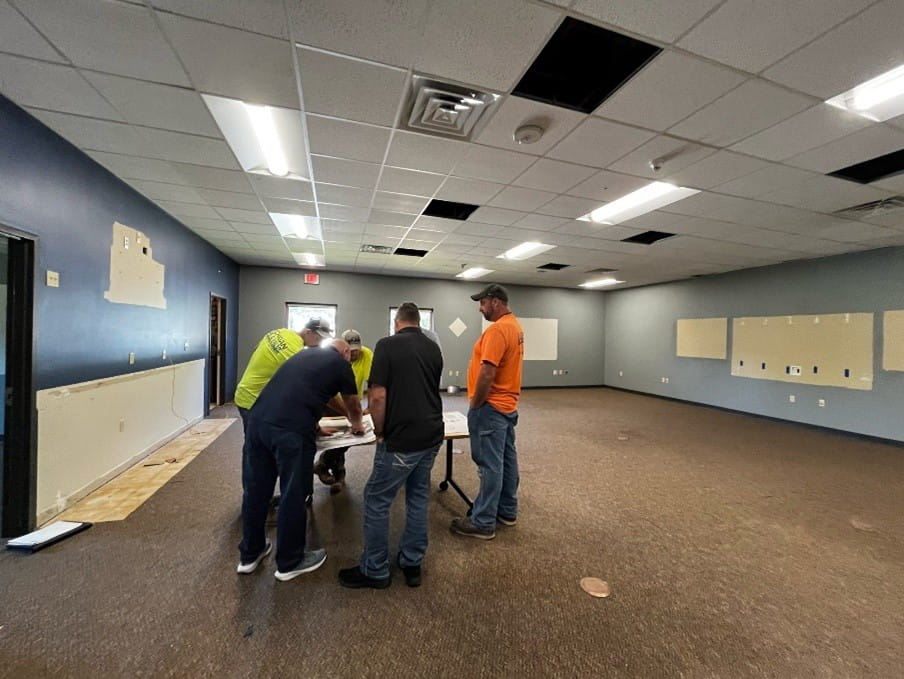 Five men huddled around a table in an empty room, looking at documents.