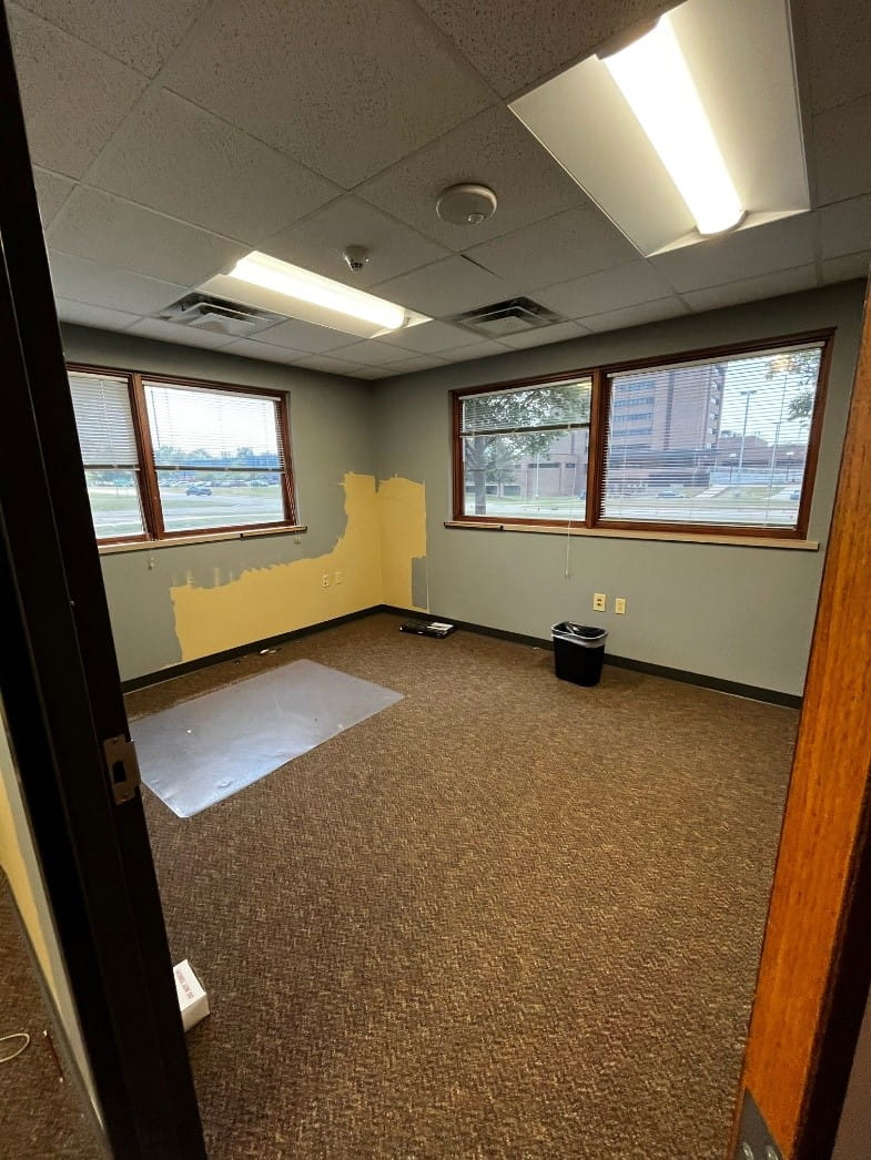 An empty office with brown carpet, grey walls and a view of the MSP Training Academy out the window. 
