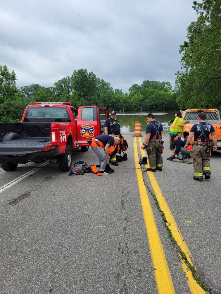 Several first responders stopped in a road, preparing to go into flood water. 