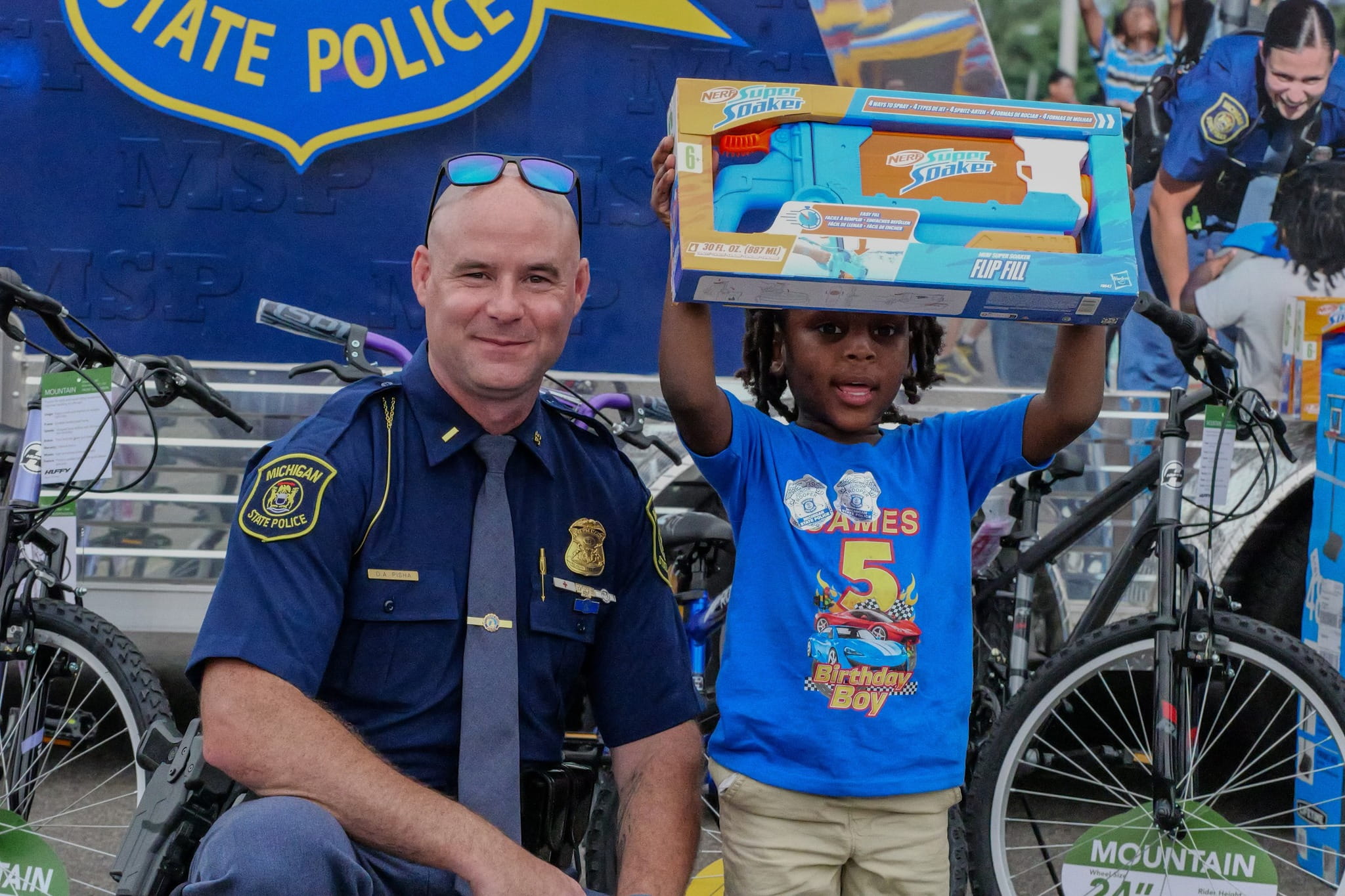 MSP lieutenant posing with young boy who holds a Super Soaker water toy overhead. 