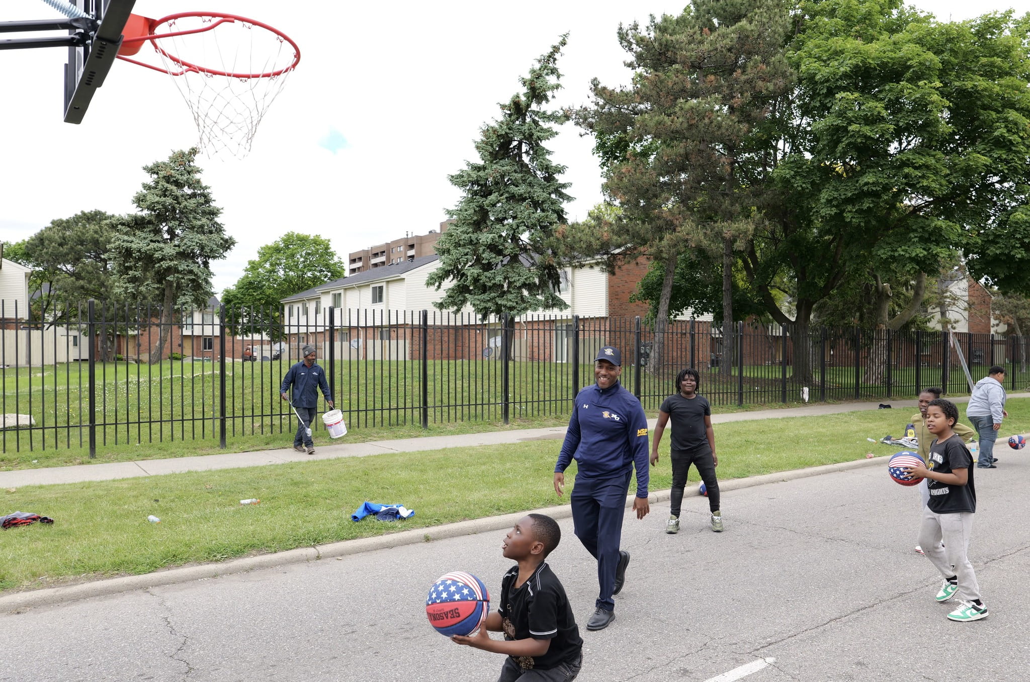 Police officer and children playing basketball outdoors. 
