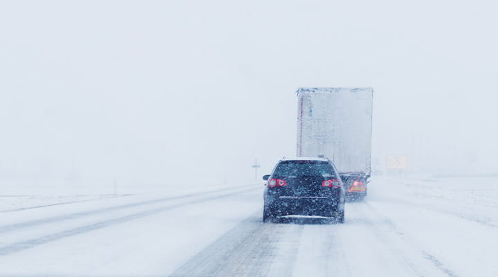 Car following large truck on snowy road. 
