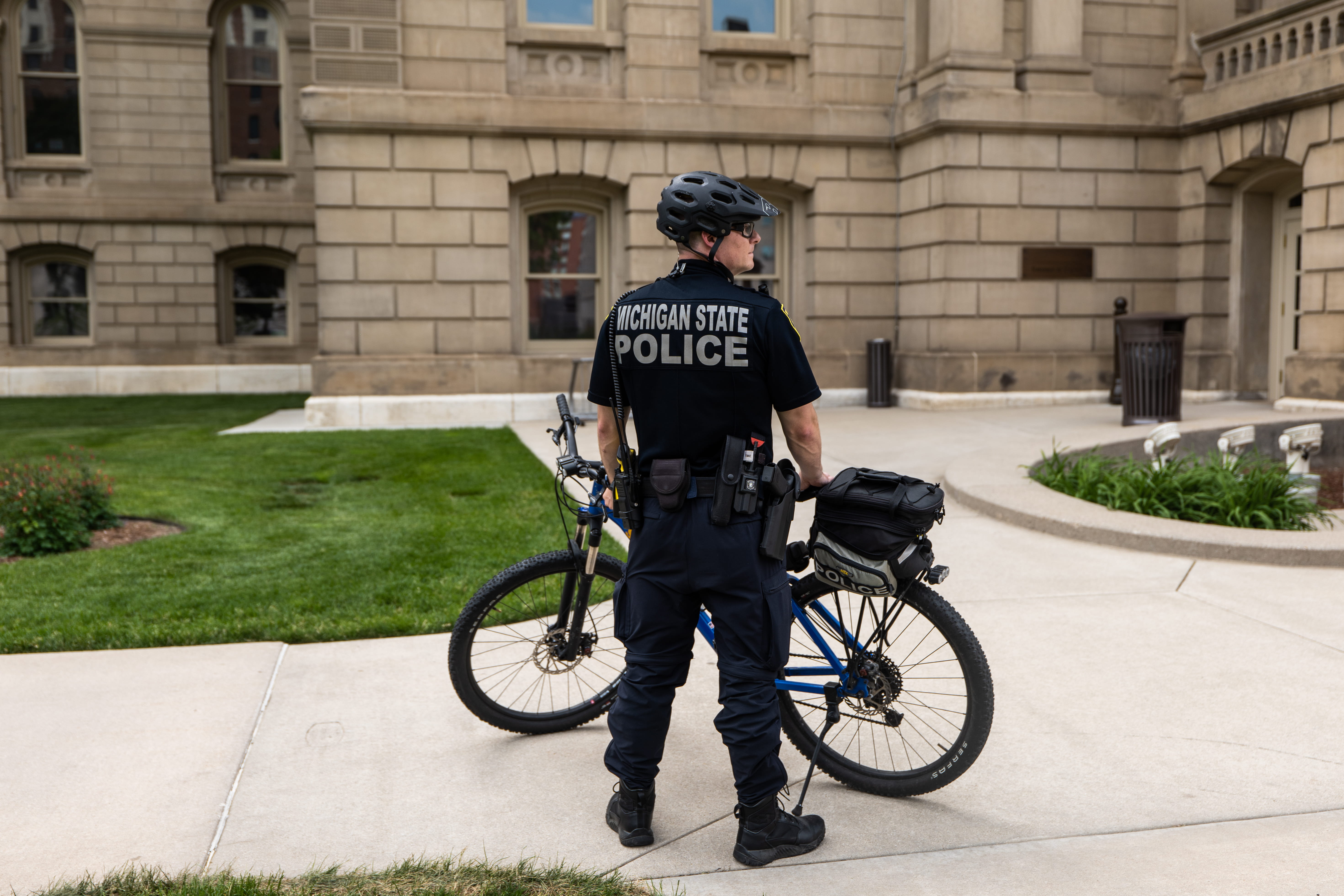 State Properties Security Officer standing outside Capitol with bicycle, wearing helmet. 