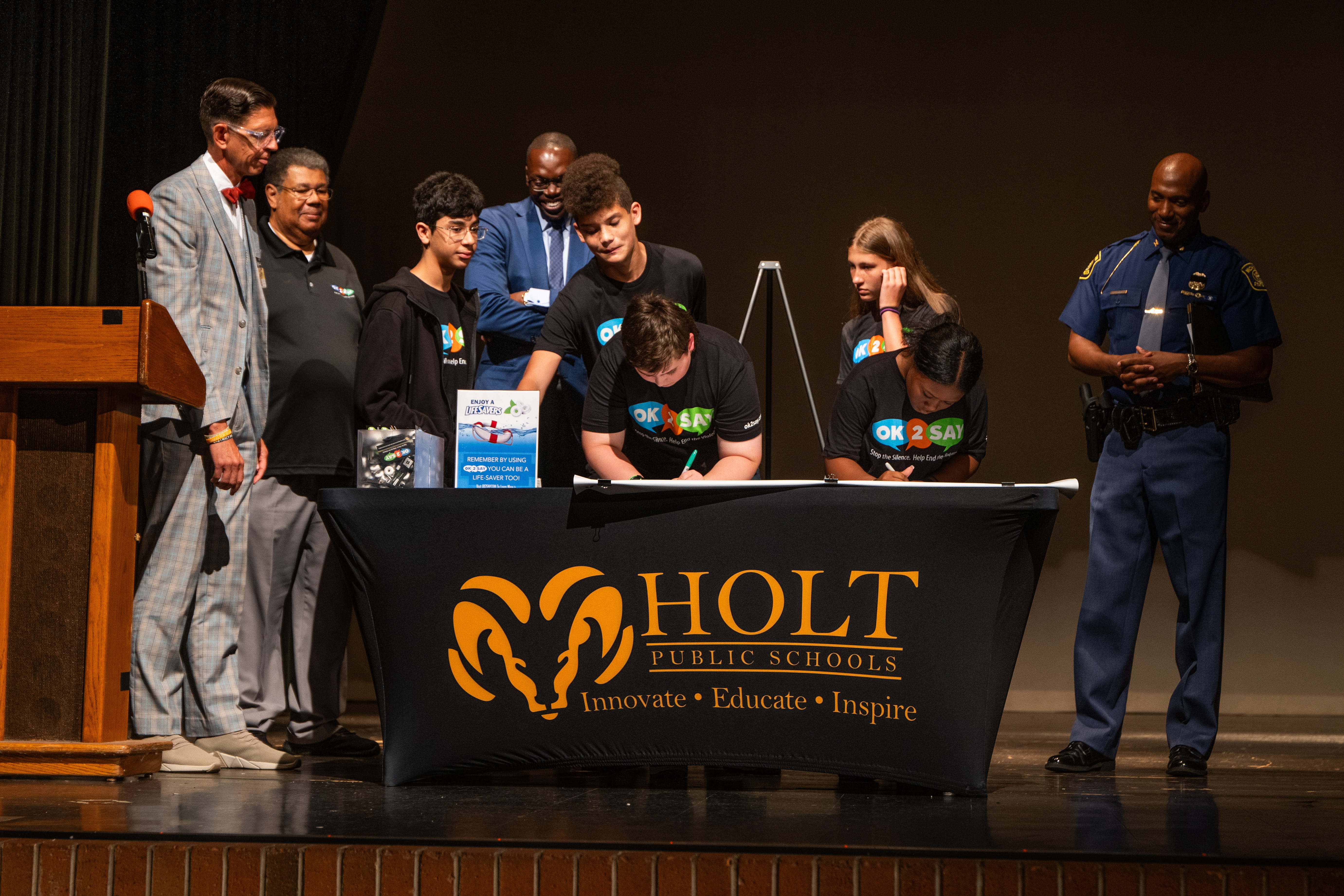 Holt Junior High student signing the OK2SAY pledge banner on auditorium stage 