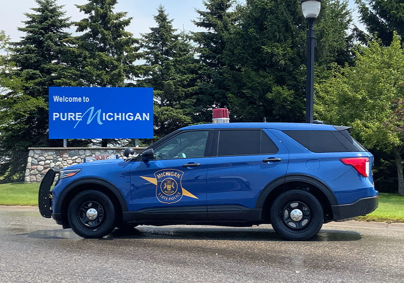 MSP patrol car in front of Welcome to Michigan sign. 