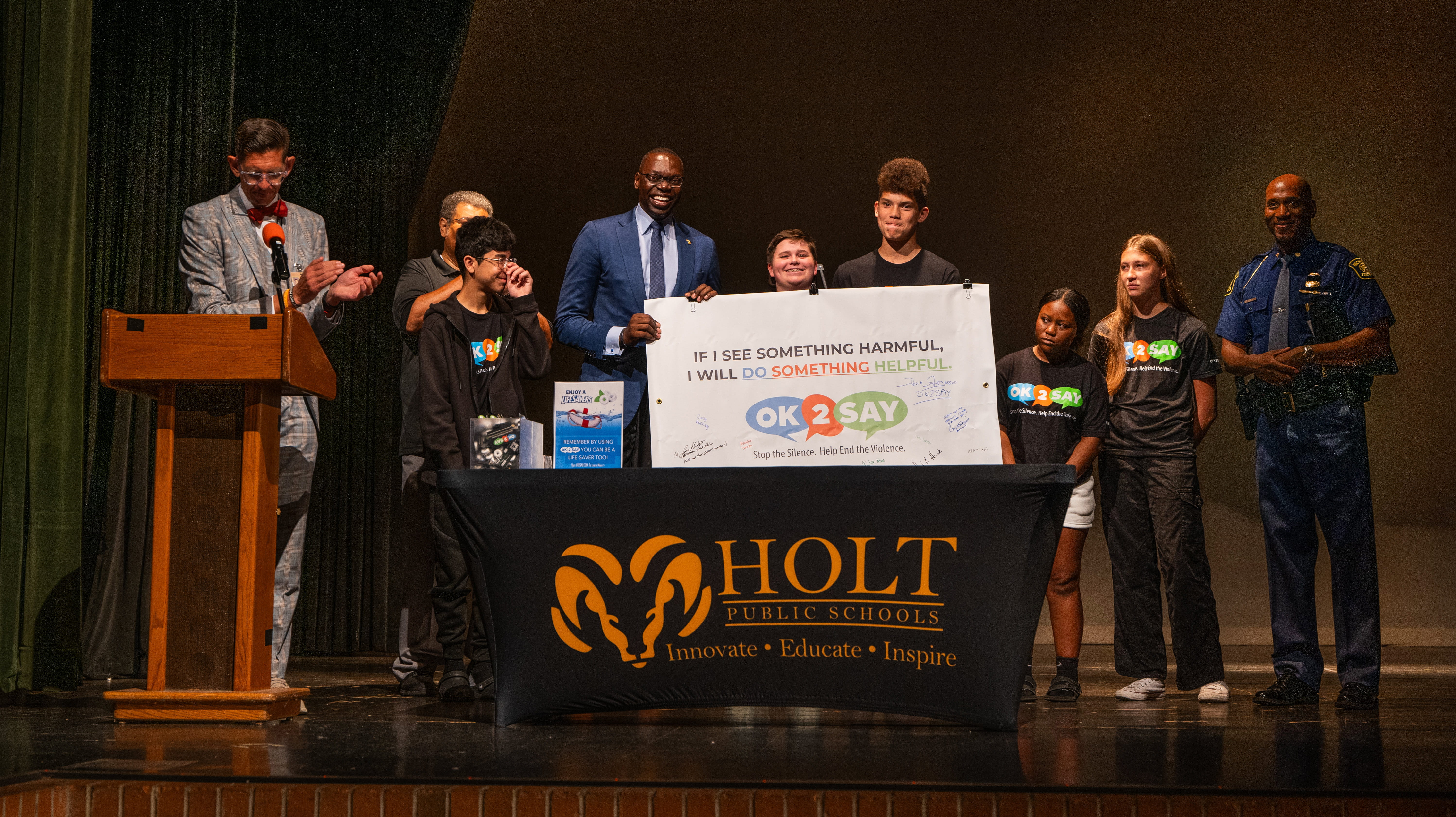 Lt. Gov. Garlin Gilchrist and Col. James F. Grady II with students and Holt Public Schools Superintendent holding an OK2SAY pledge banner