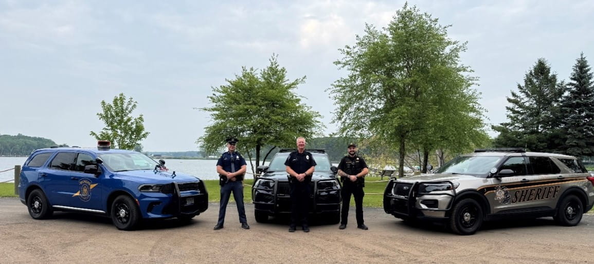 Three men in uniform standing in front of their patrol vehicles outside