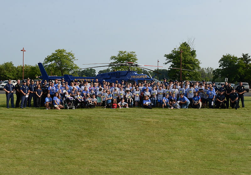 Group photo of kids and police at Sunny Day Camp in Lapeer, standing in front of the MSP helicopter