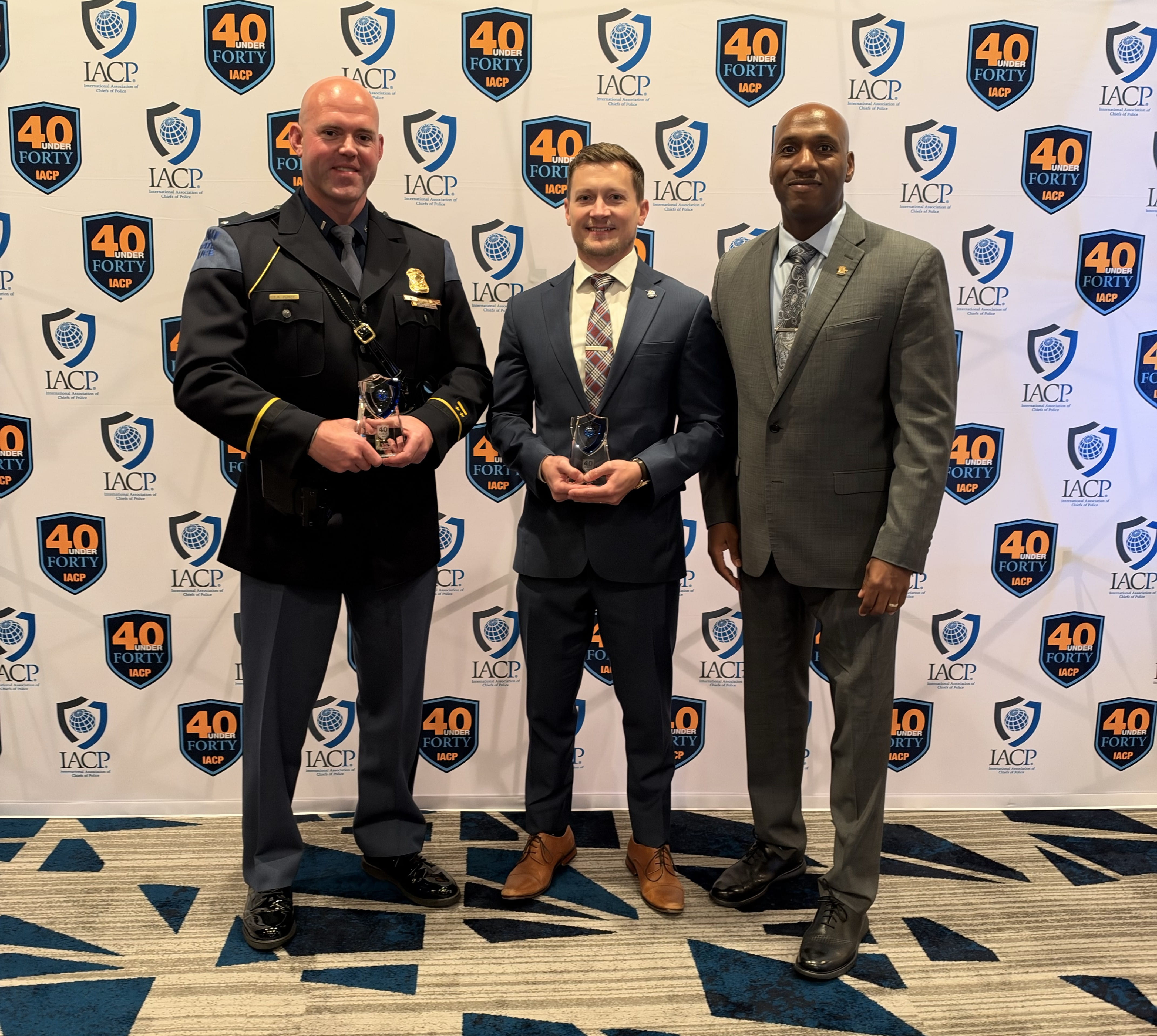 Left to Right, standing inside holding awards are First Lieutenant Ty Purdy and Mr. Eric Fowler with Colonel James F. Grady II