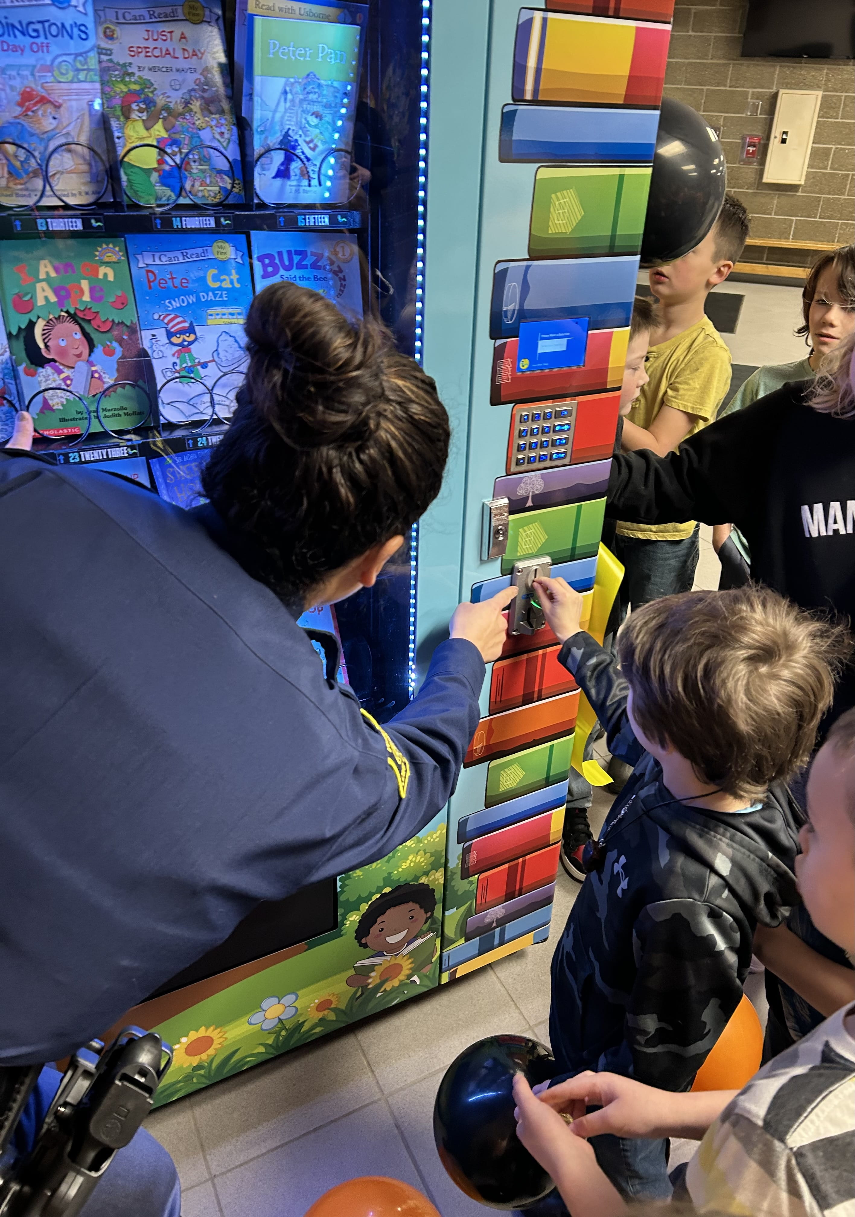Trooper at children using a book vending machine at Mancelona Elementary School
