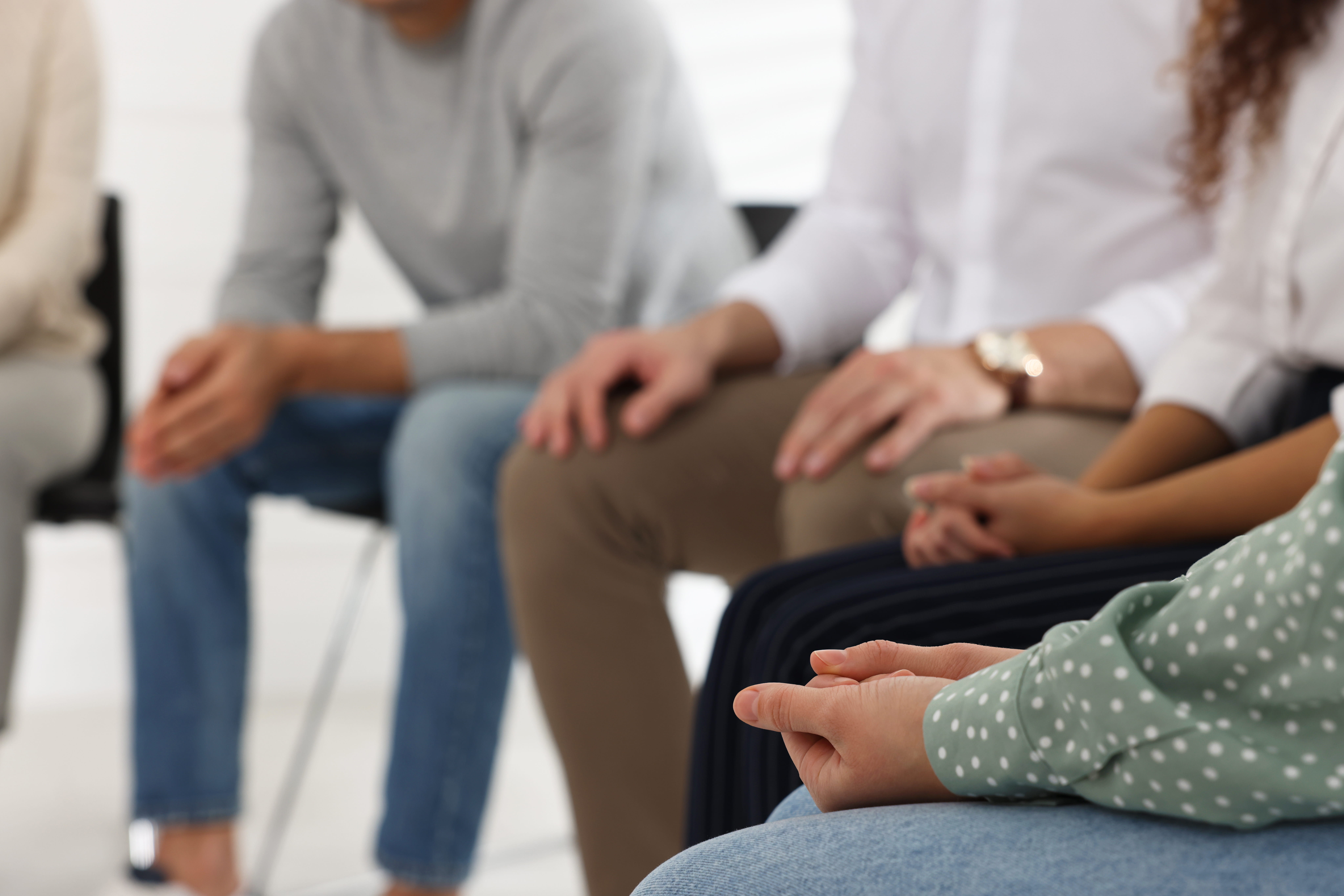 Group of women and men, picture from the shoulders down, sitting in a circle reminiscent of group therapy