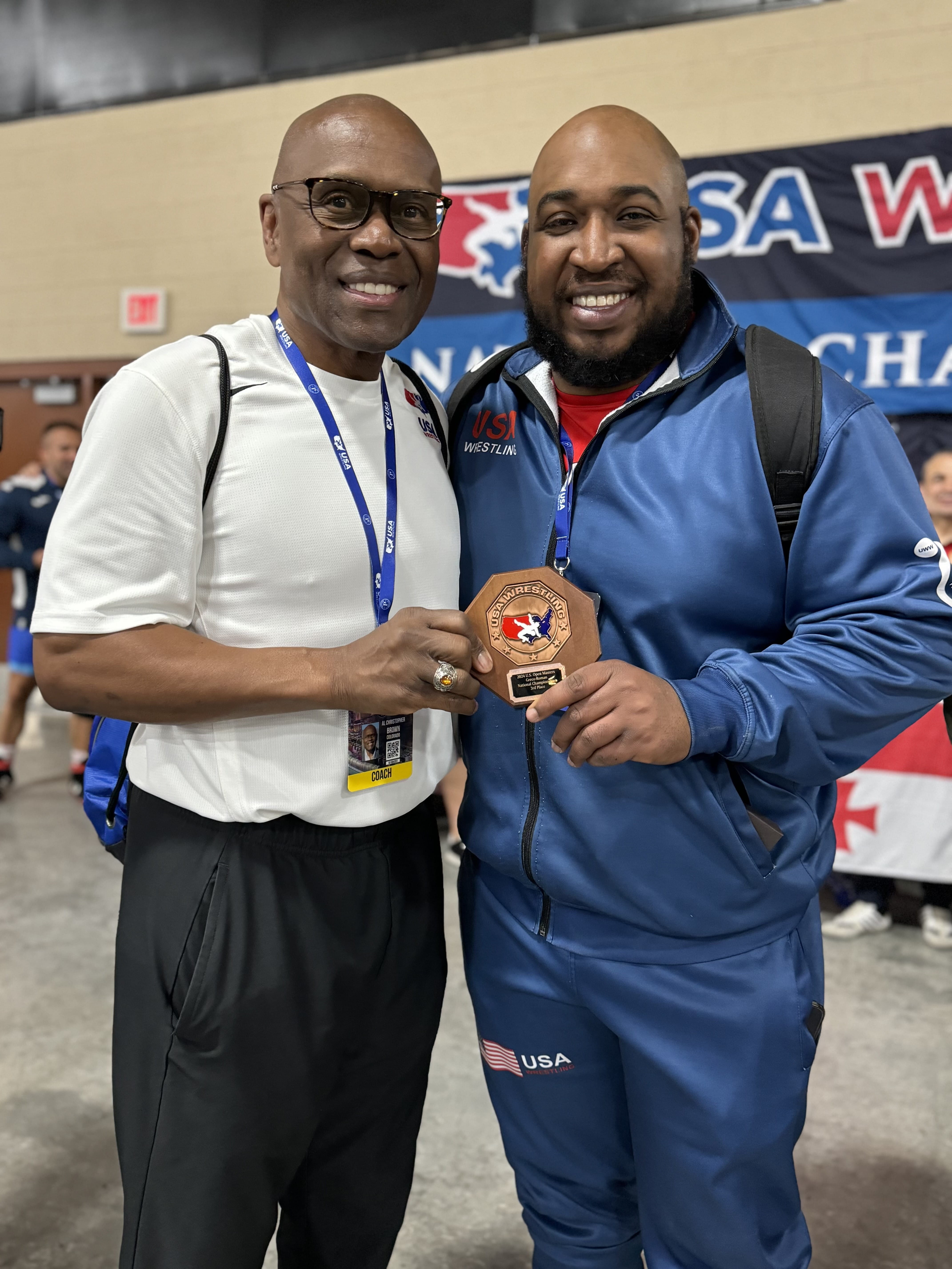 Man and Raymone Gude standing inside a gym with Gude holding a medal