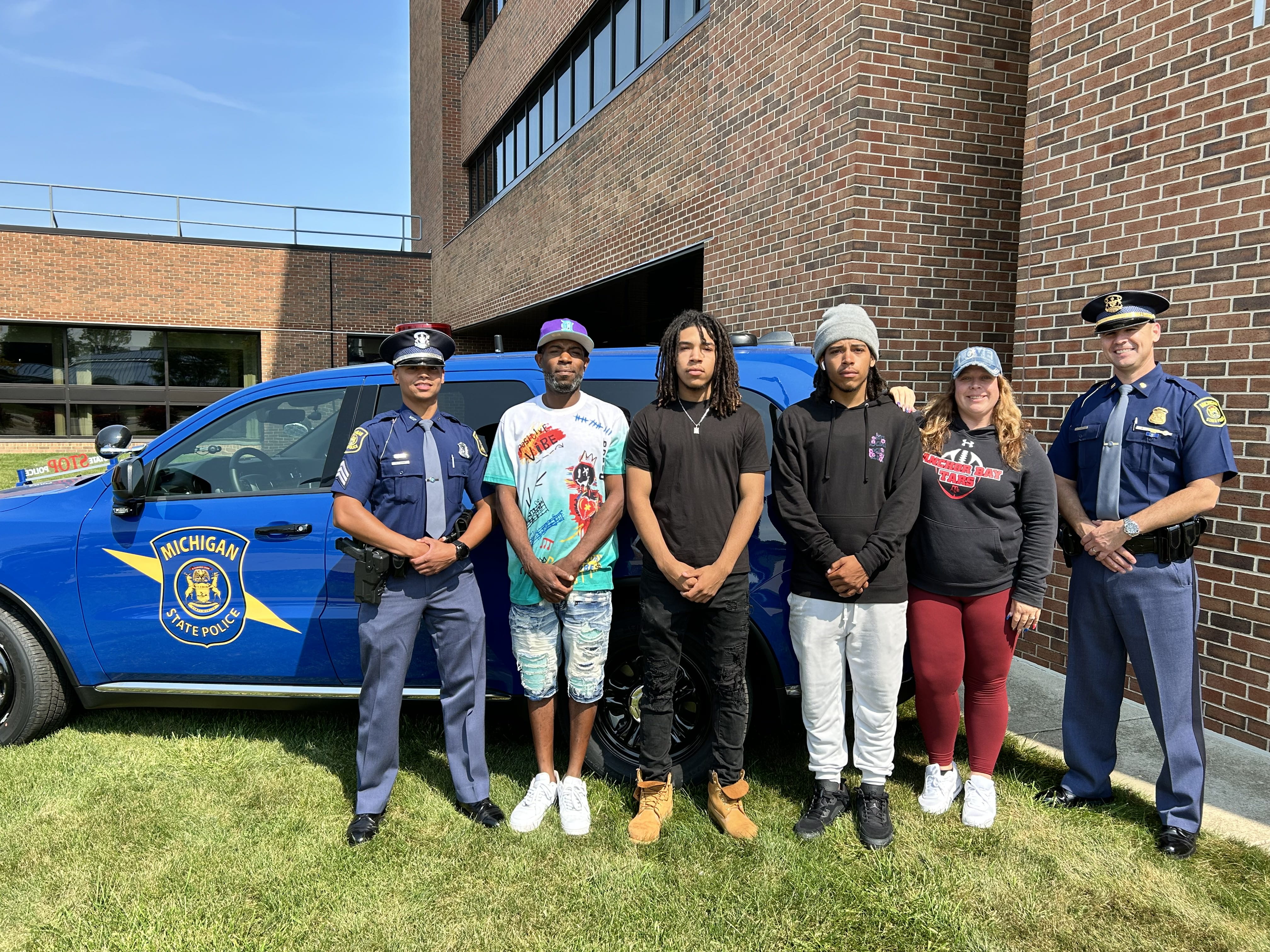 Sgt. Dijon Ware; Bryson Horton with sons Demontray and Devon; their mother, Crystal; and Capt. Greg Morenko standing in front of a patrol vehicle