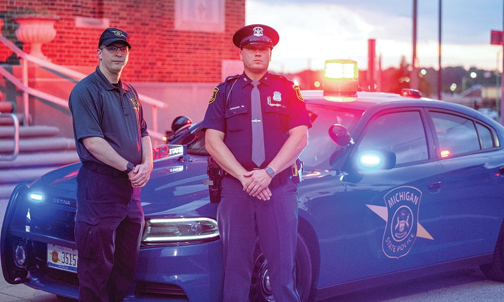 photo of Father Anthony Strouse and Trooper Mark Swales standing in front of a patrol car