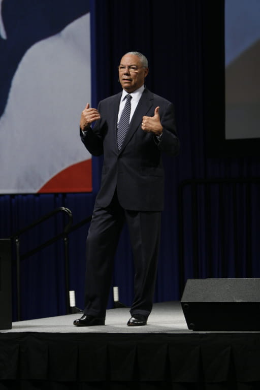 Colin Powell standing on stage with a microphone speaking in 2007