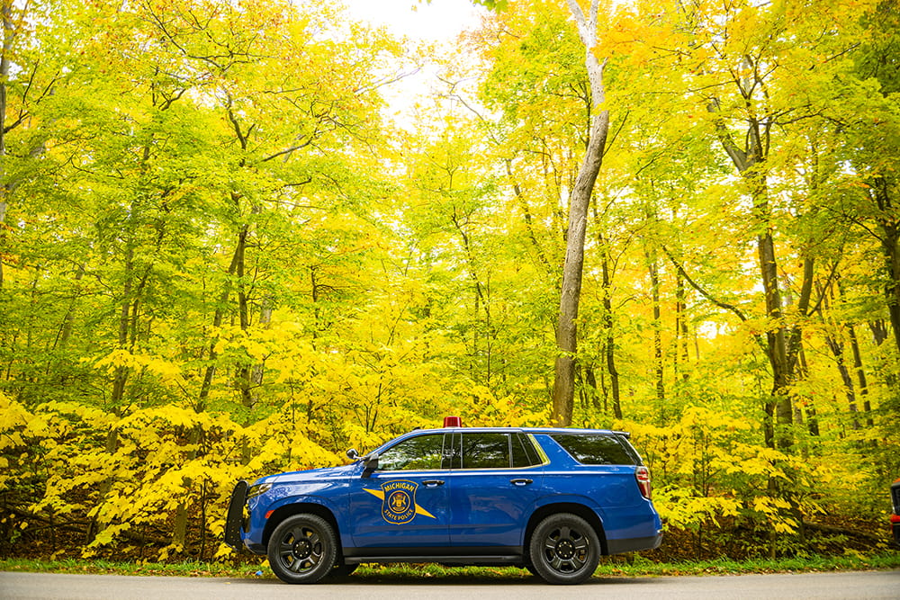 Michigan State Police patrol car parked in front of forest of bright green and yellow leaves.