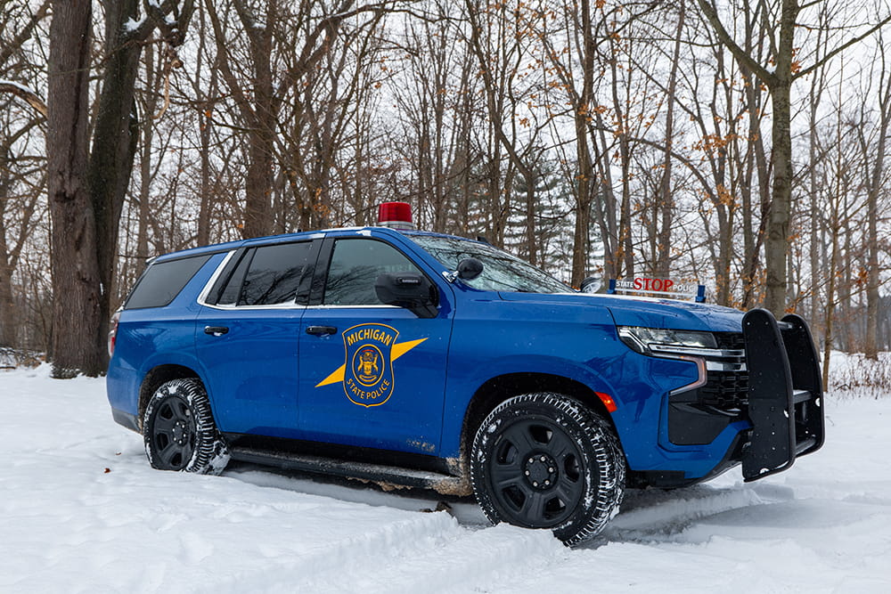 Sideview of Michigan State Police patrol car, in snow with bare trees in background.