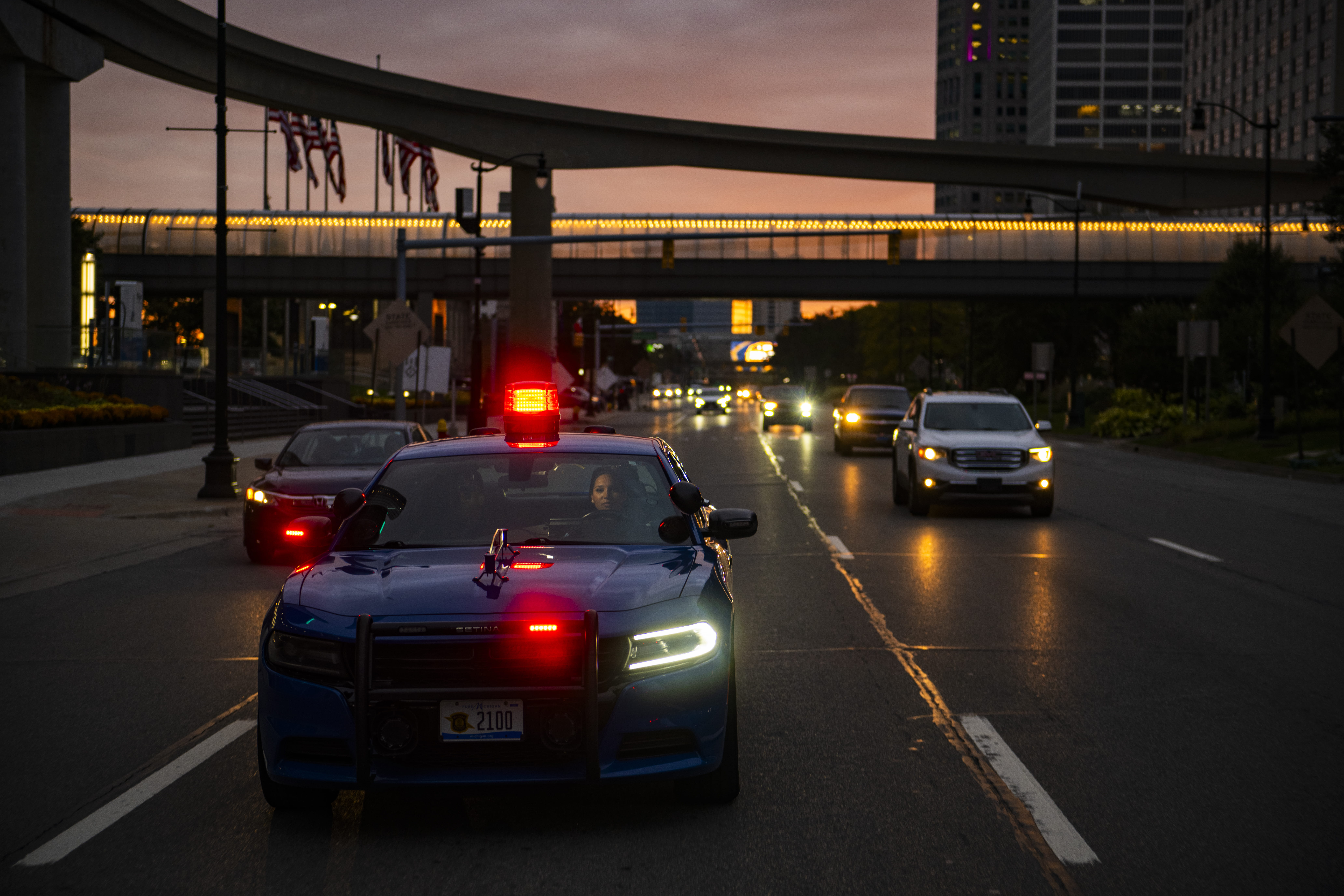 Trooper driving patrol car in city at dusk.