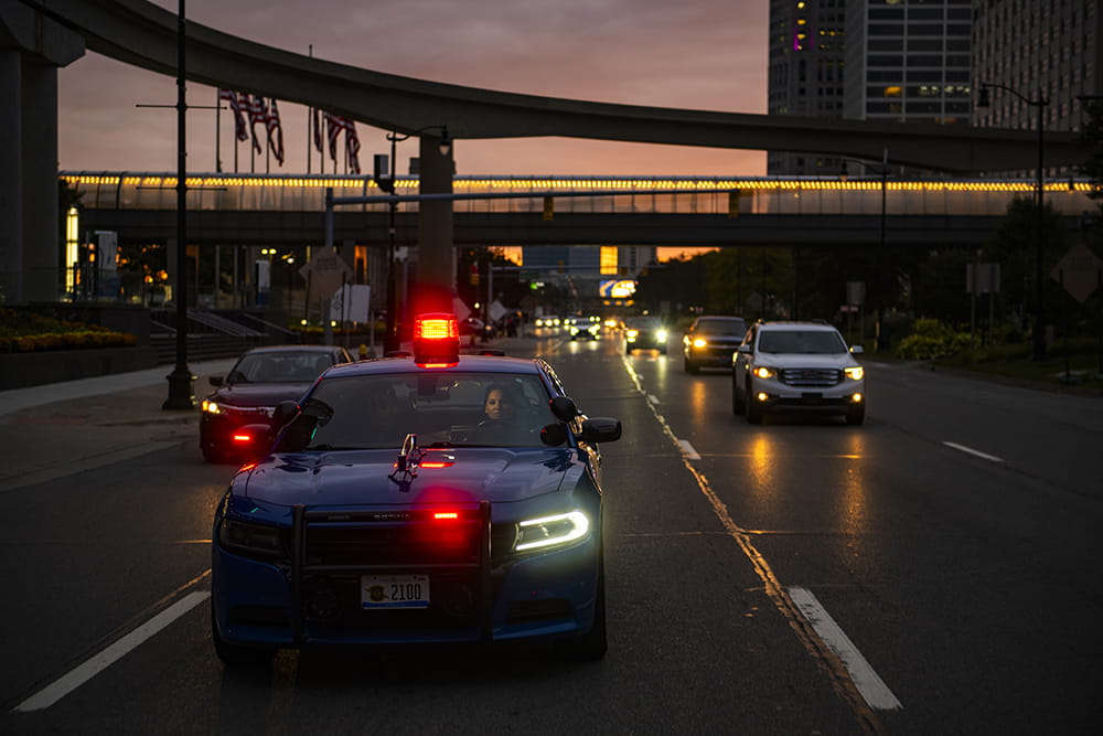 Trooper driving patrol car in city at dusk.
