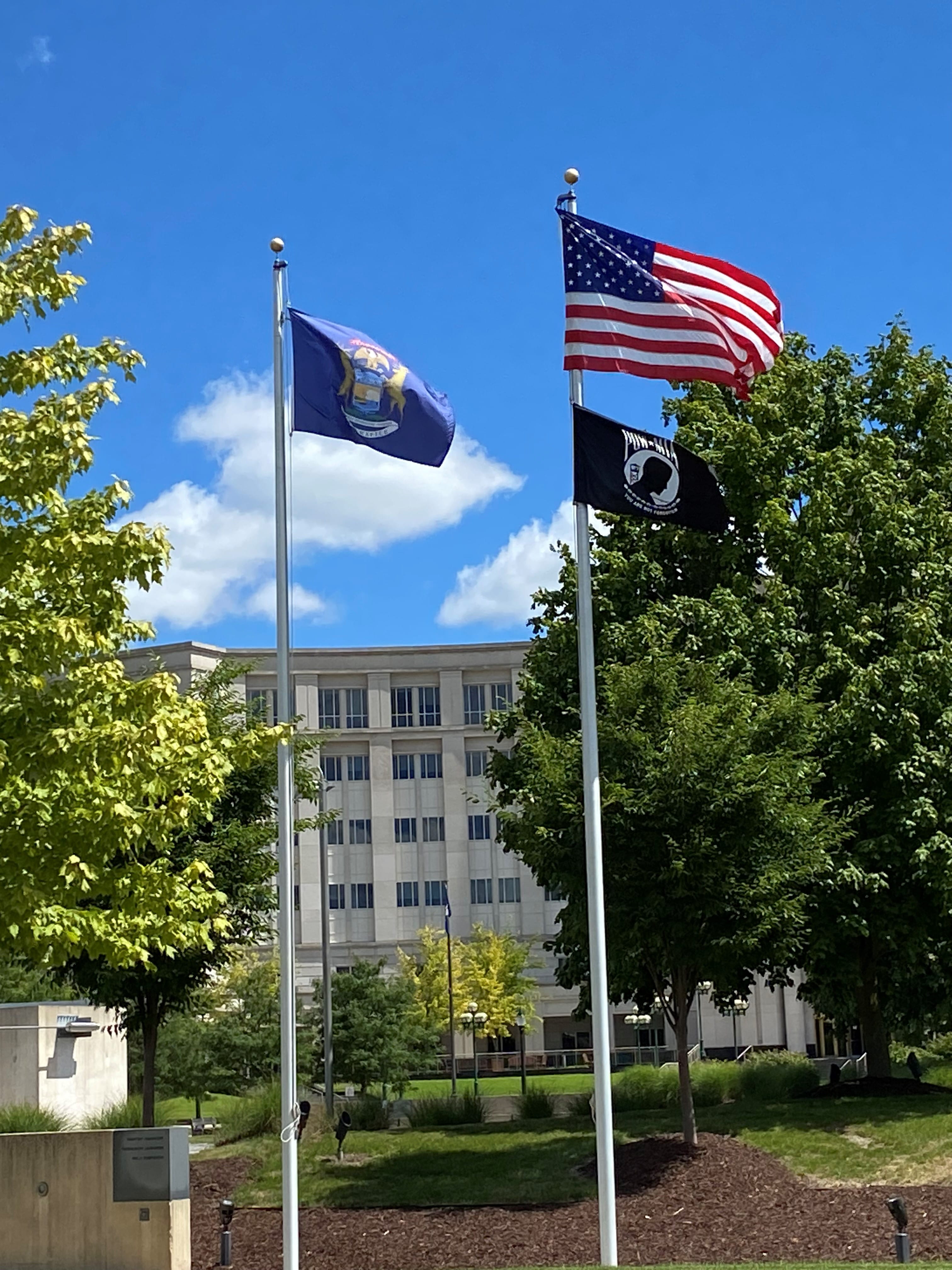 USA flag. State of Michigan flag, and POW flag at full mast in the park