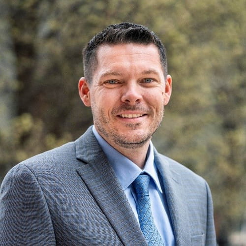 Headshot of Todd Buter in a gray suit with blue shirt and tie