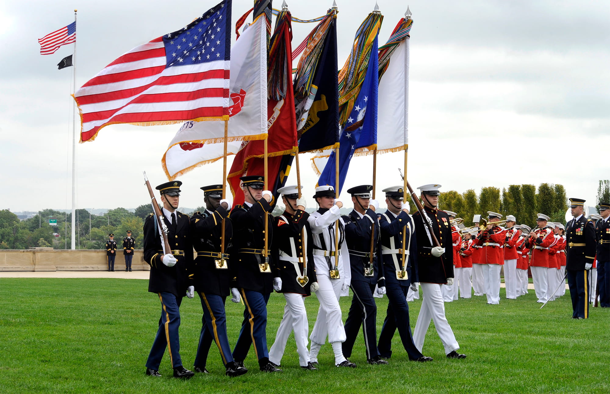 Image of 8 individuals in dress blues carrying flags