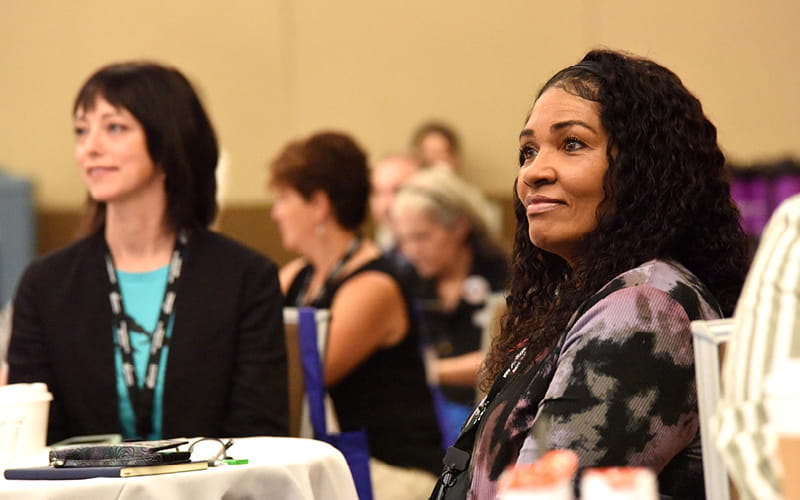 women seated at a table listening to a speaker at a conference
