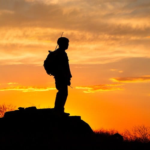 Soldier standing on mountain with sunset in background