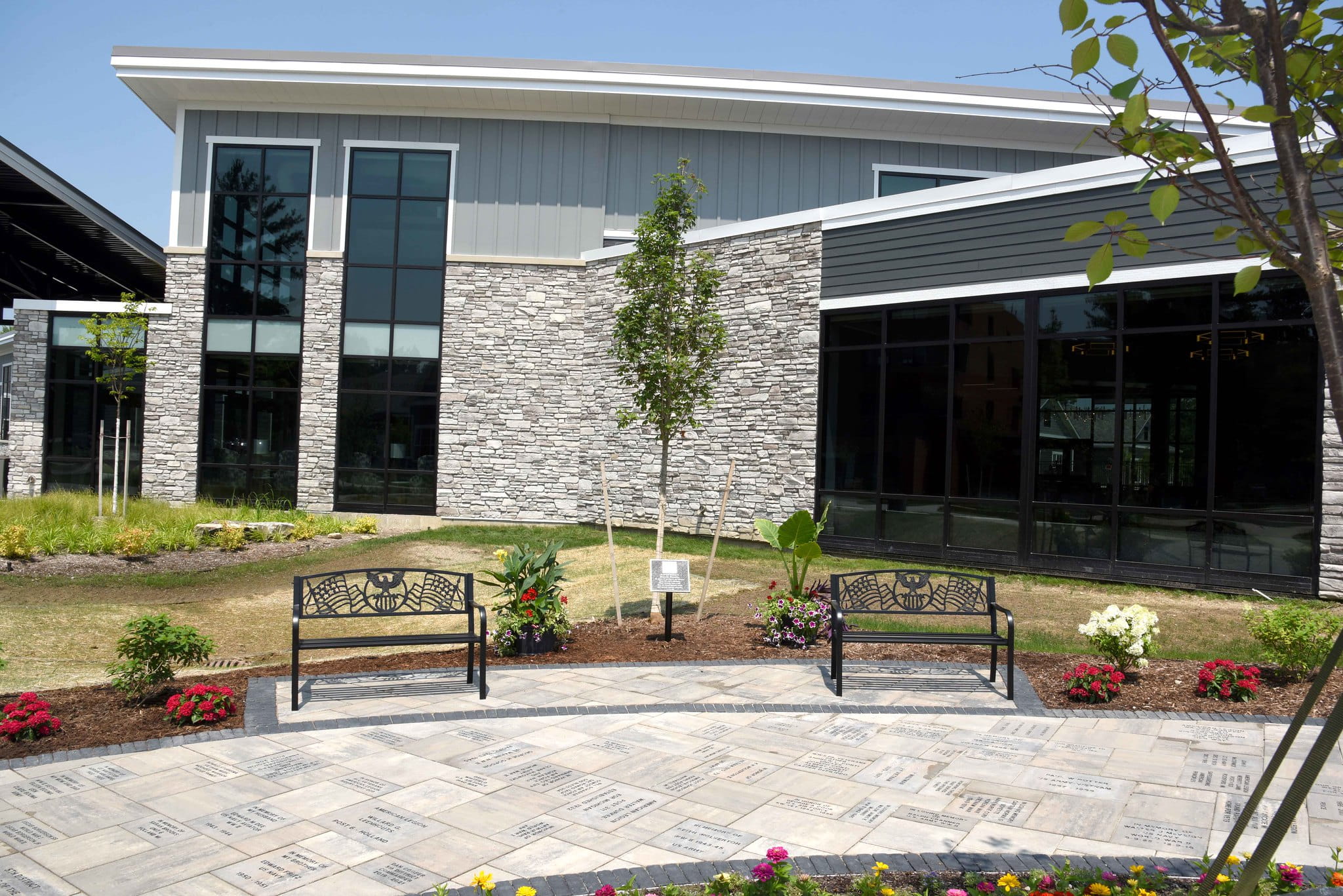 Memorial garden with two park benches, tree and landscaping around entrance to Home