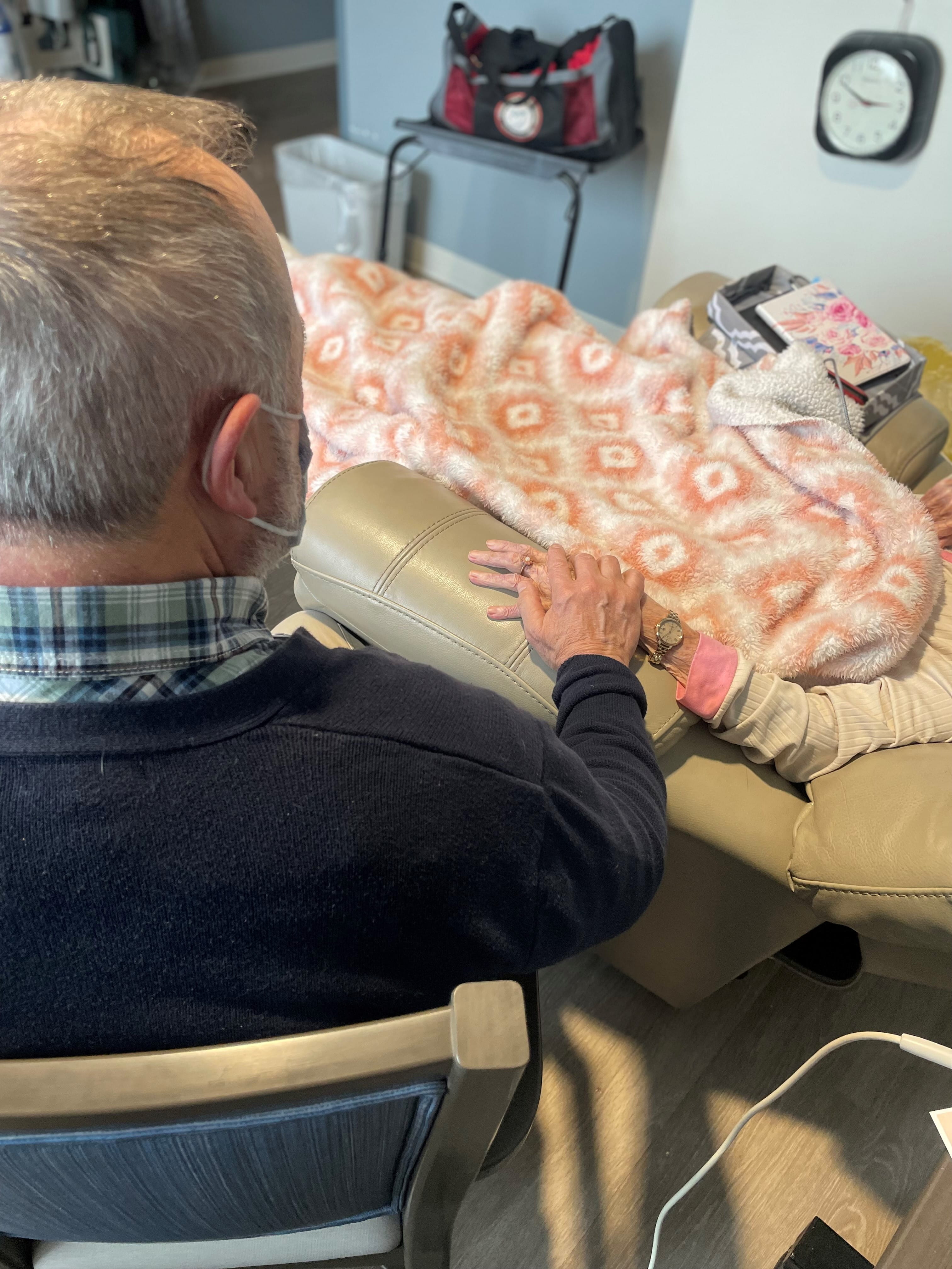 Man sitting next to hospital bed holding woman's hand