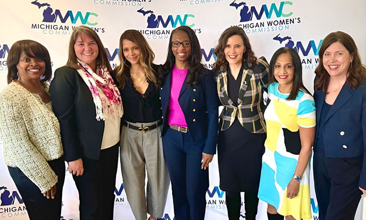 Commissioners stand with actor Halle Berry and Gov. Gretchen Whitmer in front of a backdrop with repeated pattern of MWC logo