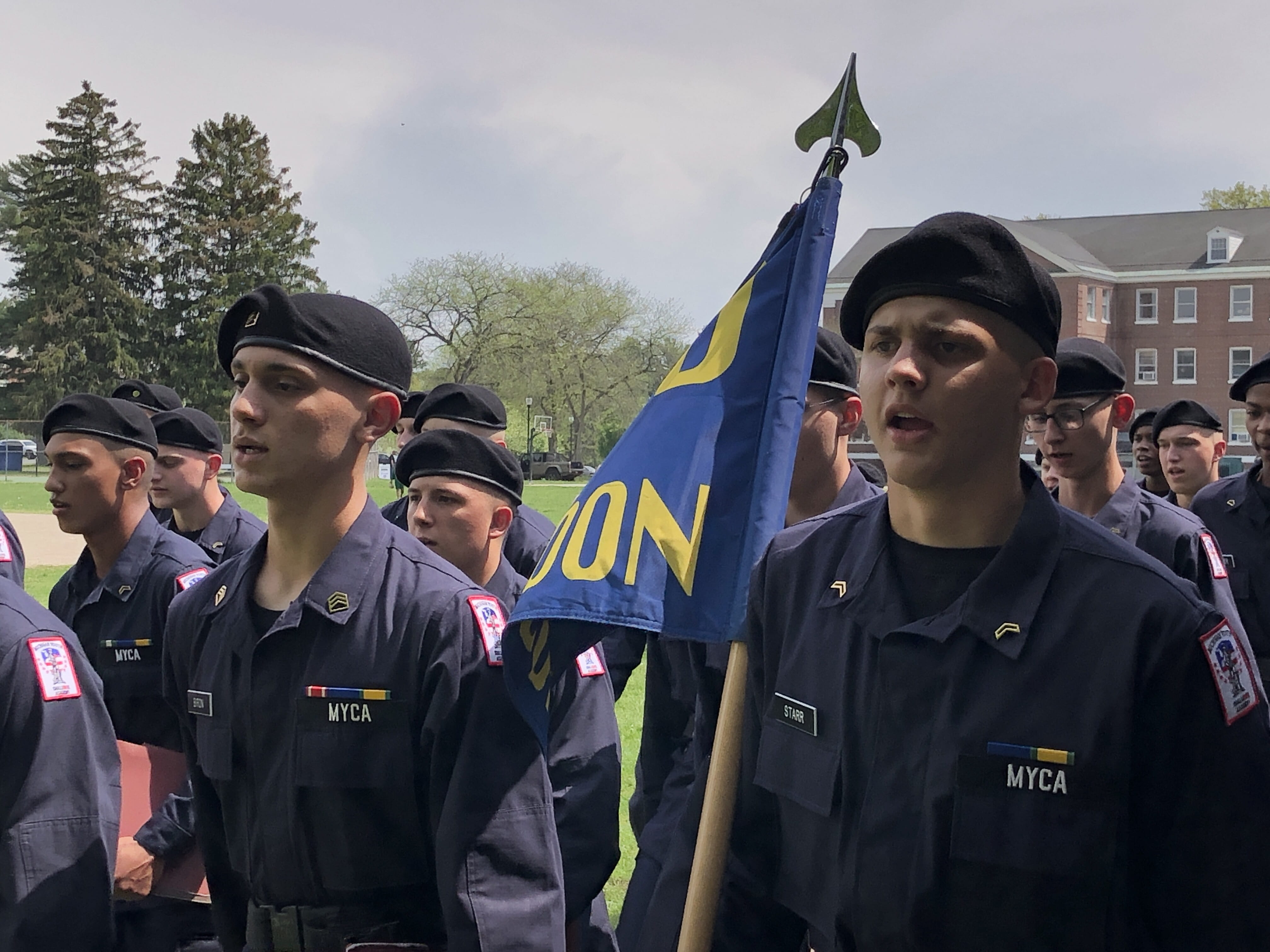 Group of male cadets marching while carrying flag