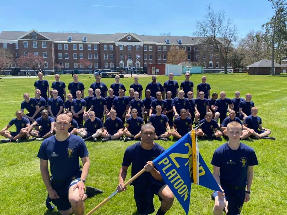 Cadets sitting on a grass lawn and posing for a picture.