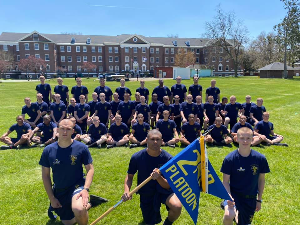 Cadets sitting on a grass lawn and posing for a picture.