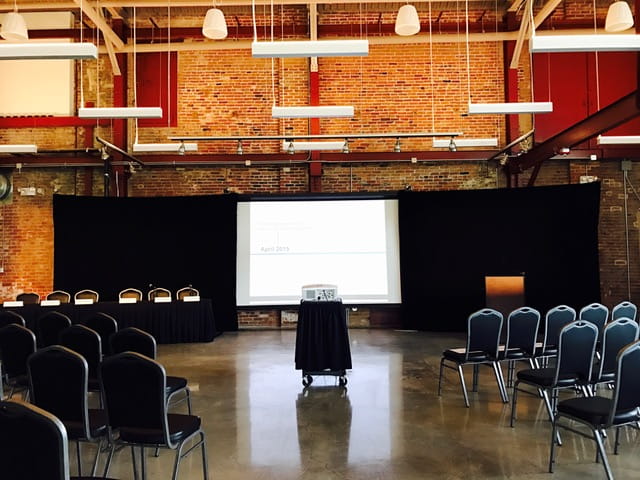 The OAC's Riverview Loft room set up for a meeting with projector, screen and rows of chairs.