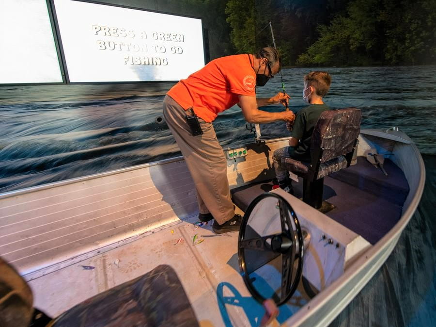 OAC staffer helps young boy use fishing simulator