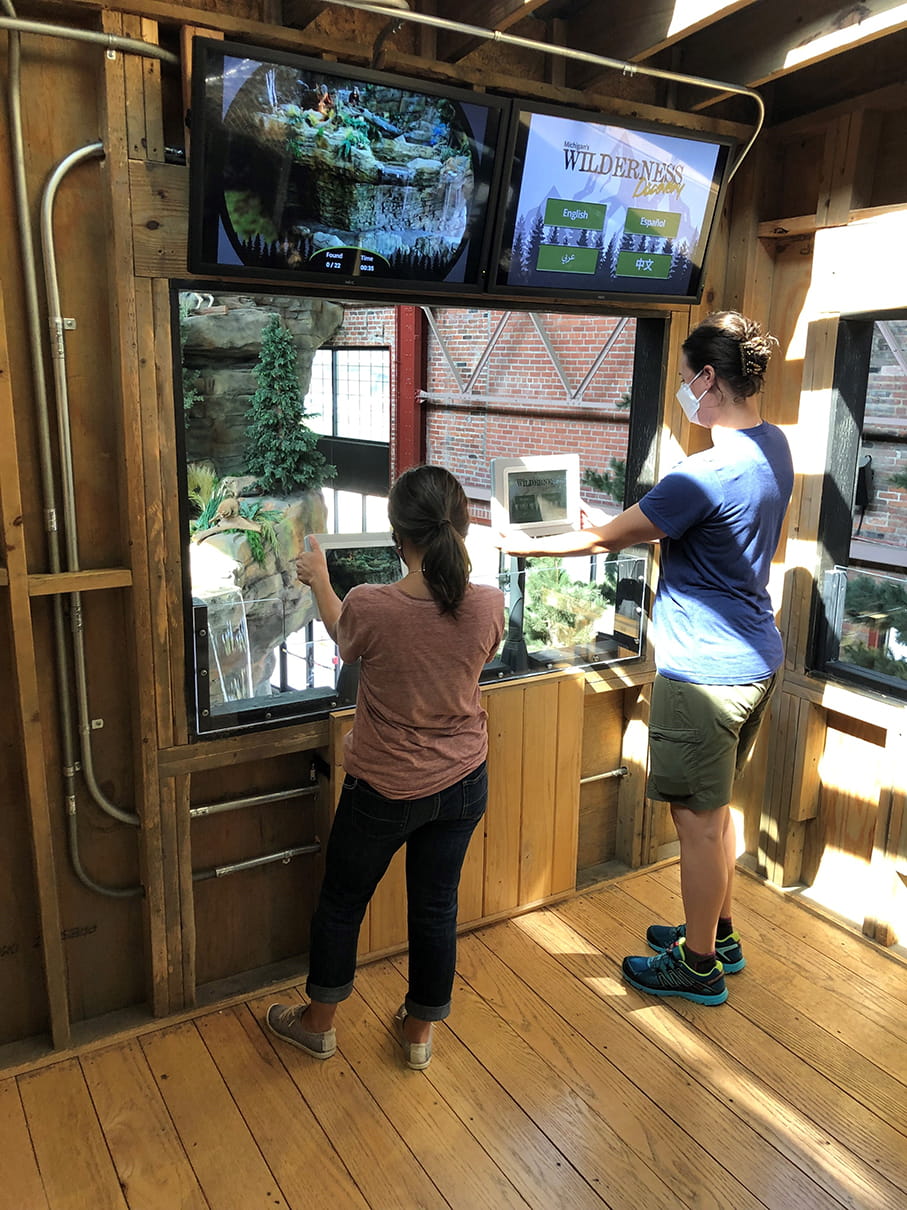 Two teenage girls using Wilderness Discovery app on tablets in OAC tower blind exhibit