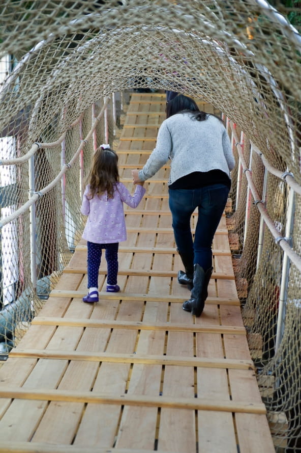 mom holds little girl’s hand as they cross the suspension bridge at the Outdoor Adventure Center