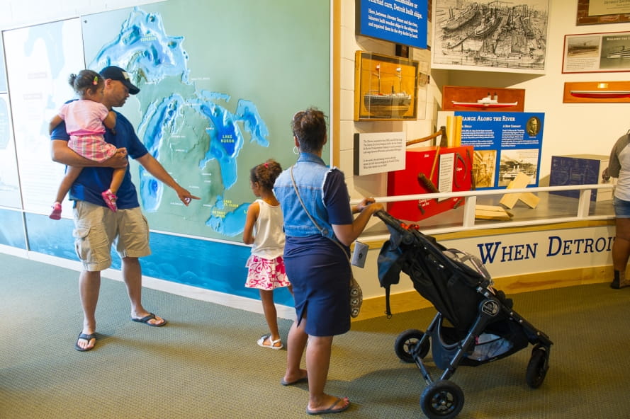 Family looks at map of Michigan in Outdoor Adventure Center exhibit about shipping and Detroit River