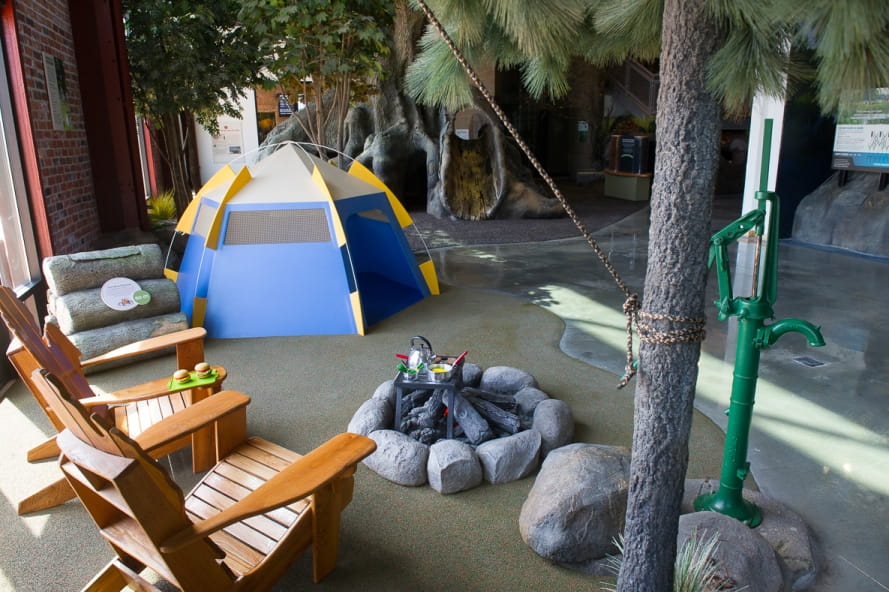 Outdoor Adventure Center campsite exhibit, with tent, campfire, chairs, tree
