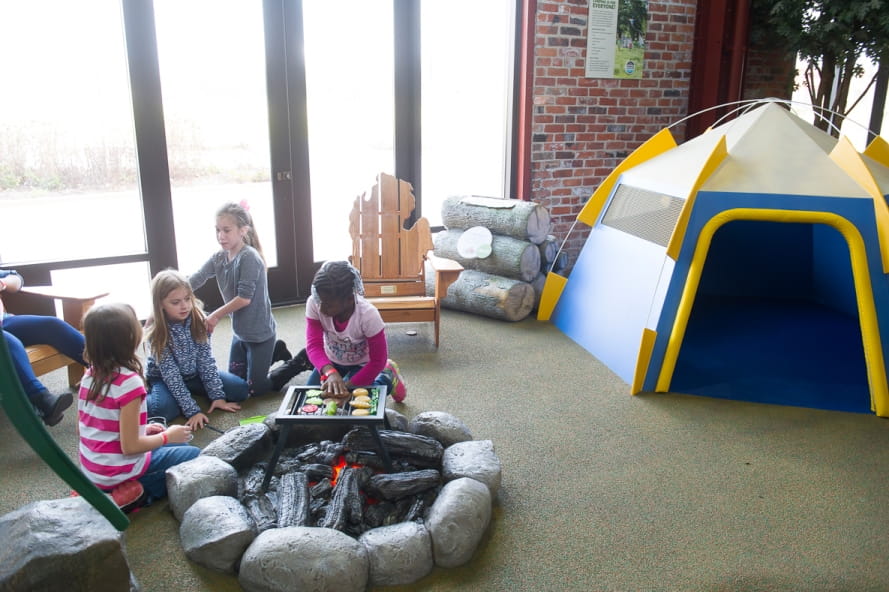 group of girls plays by campfire in Outdoor Adventure Center campsite exhibit
