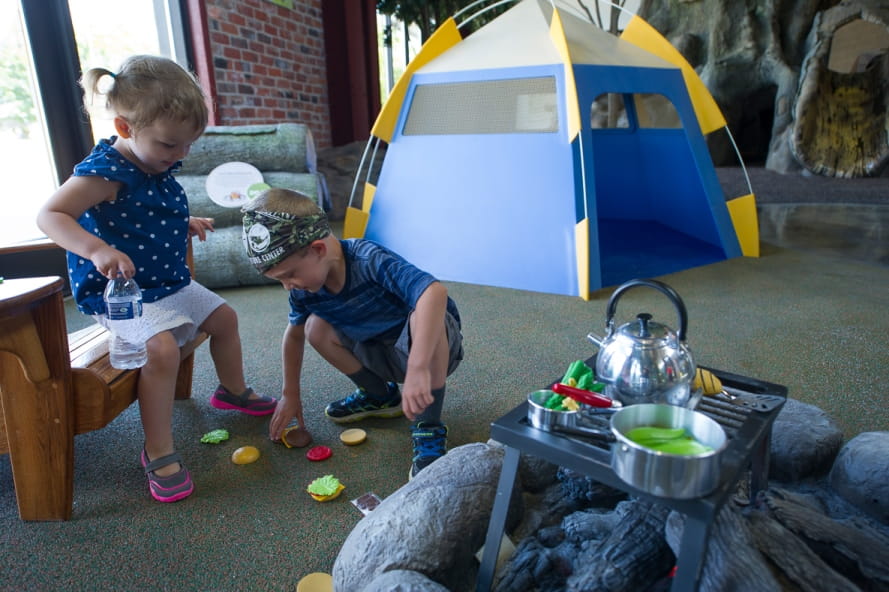 young boy and girl cooking pretend food over campfire in Outdoor Adventure Center campsite exhibit
